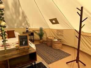 A tent with a bed, a welcome sign, a small table, wicker baskets, and a coat rack.
