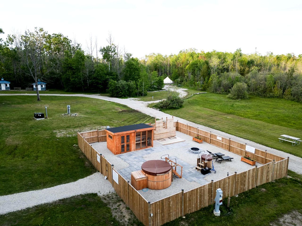 A fenced outdoor area with a hot tub, seating, and a small wooden structure.