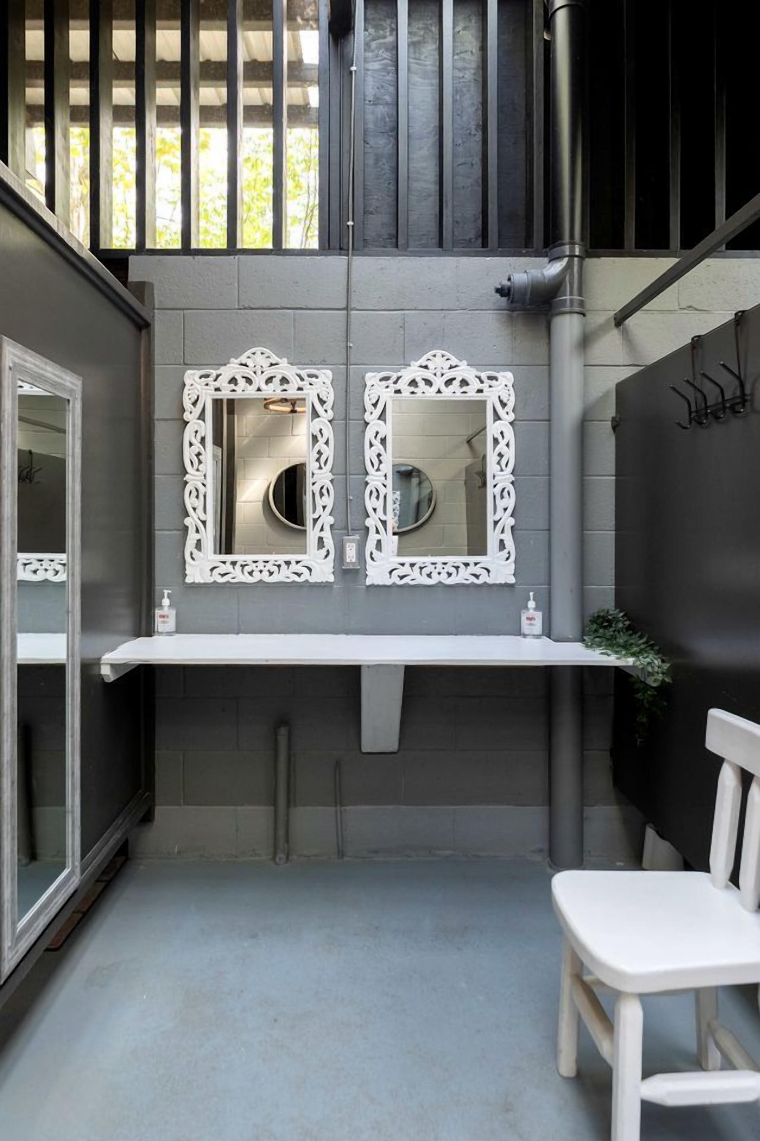 A bathroom with two ornate mirrors, a white sink, and a white chair.