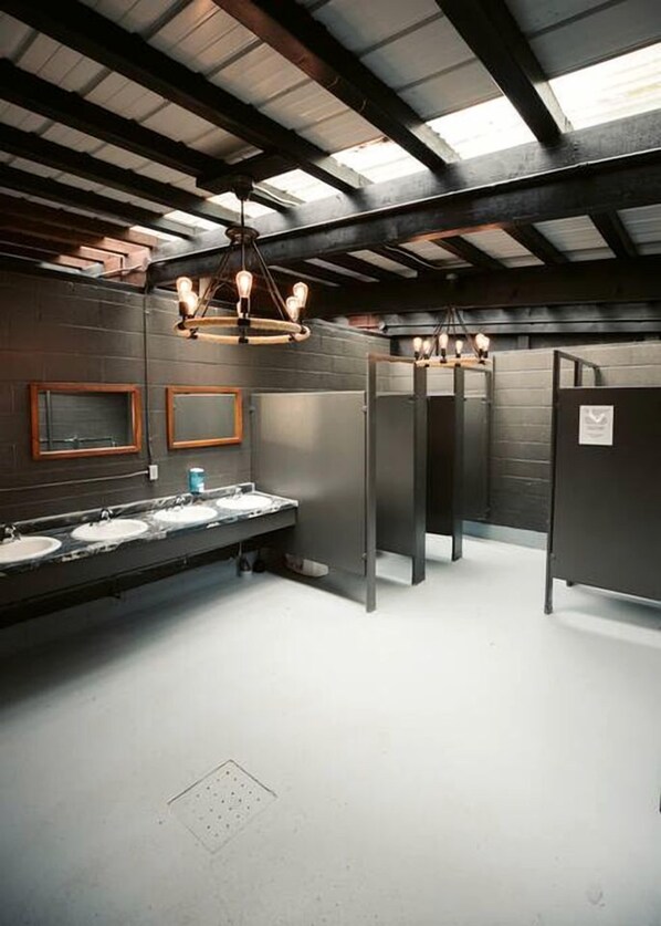 A restroom with three sinks, a mirror, and a ceiling with exposed beams.