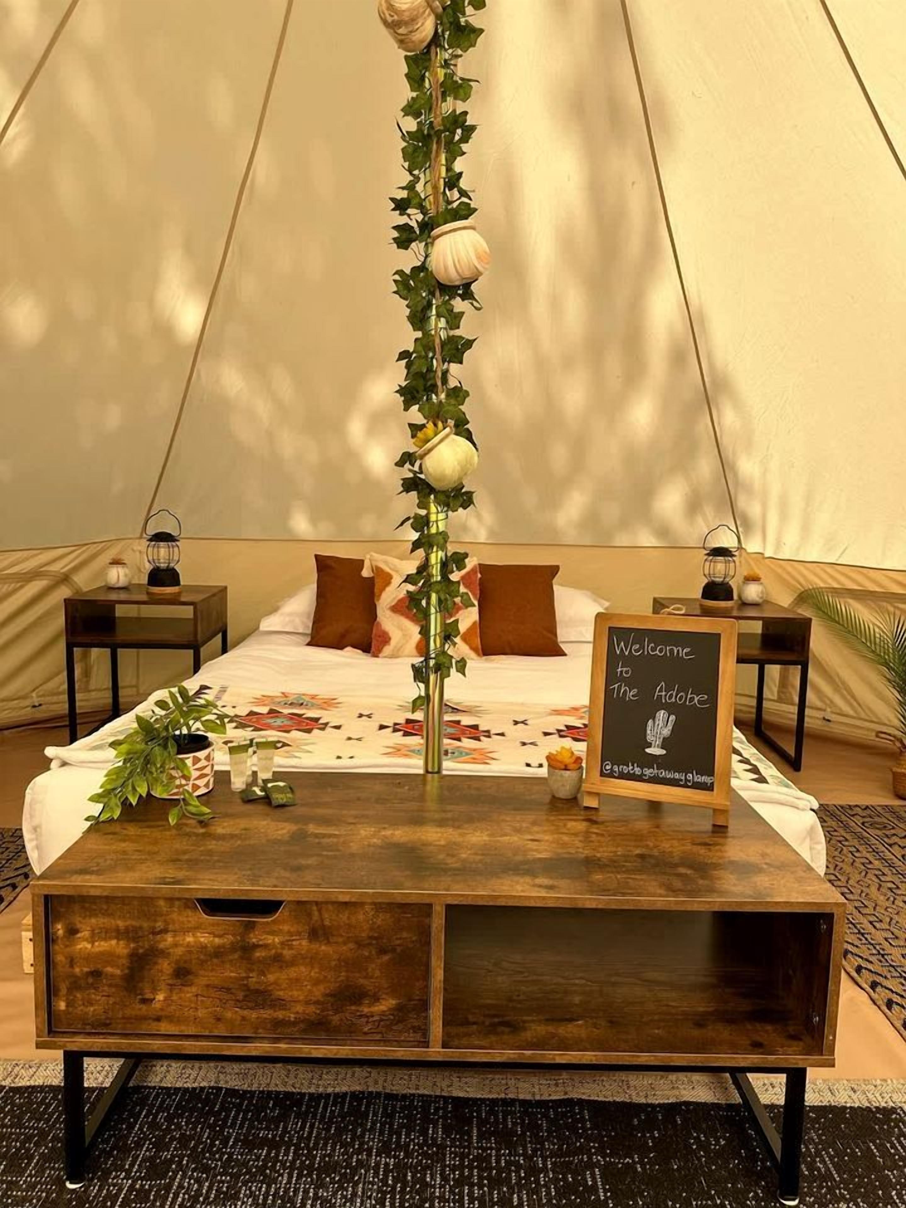 A tent with a bed, a wooden coffee table, a welcome sign, and a lantern on either side.