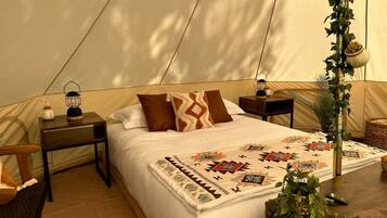 A tent-style room with a bed, bedside tables, a lamp, and a potted plant.