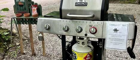 Una parrilla portátil con tanque de propano, un cartel de barbacoa y una caravana cerca.