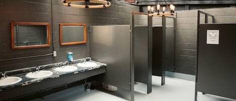 Baño con tres lavamanos, un espejo y un techo con vigas a la vista.