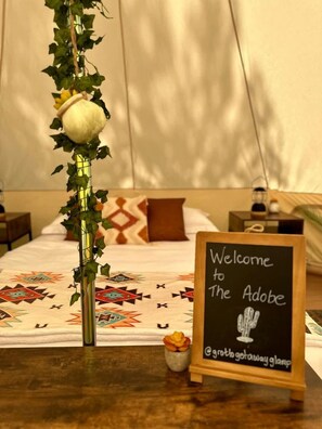 A bed with a patterned blanket, a vase with a flower, a chalkboard sign, and a small potted plant.