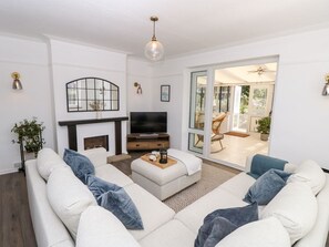 A living room with a sofa set, a television, a fireplace, and a sliding glass door leading to an outdoor area. - Topsails, Totland Bay (Freshwater)