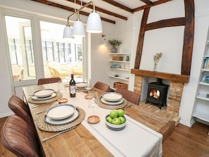 A dining area with a wooden table set for four, surrounded by leather chairs, with a fireplace and shelves in the background. - Topsails, Totland Bay (Freshwater)