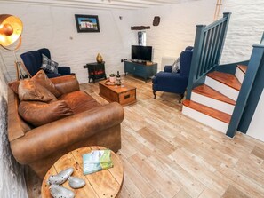 Una sala de estar con un sofá de cuero, una mesa de centro, un televisor y una escalera.