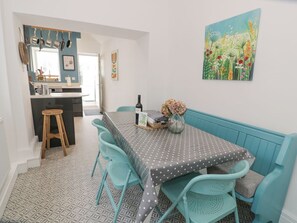 Un comedor con una mesa preparada para cuatro personas, un banco y una cocina al fondo.