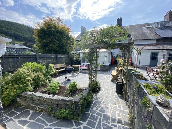 Un patio empedrado con cerca de madera, una pérgola y un jardín con plantas.