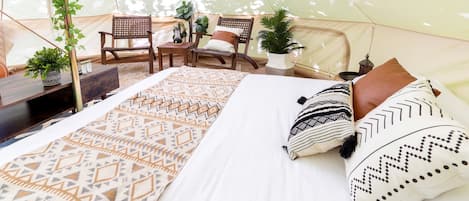 A tent with a bed, two chairs, a table, and potted plants.