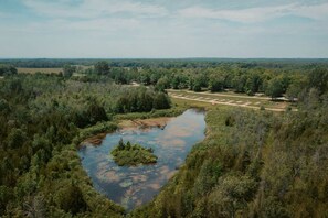 A natural landscape with a pond, dense forest, and a distant road. - Romantic Glamping Retreat: Pretty Bell Tent near Tobermory, Canada (Northern Bruce Peninsula)