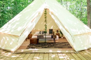 A tent with a bed, a table, and a hanging plant.