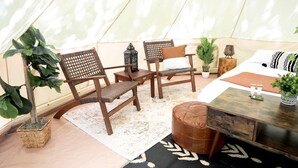 Um quarto com tenda, duas cadeiras de madeira, uma mesa pequena, um banco e uma cama com colcha estampada.