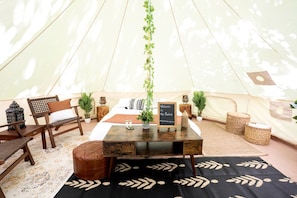 A tented accommodation with a central table, seating area, and a sign welcoming guests.