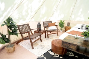 Una habitación con toldo, dos sillas de madera, una mesita, un banco y una cama con colcha estampada.