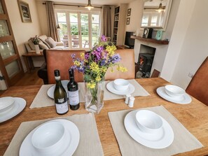 Une table à manger dressée avec de l’assiette, des bols et des couverts blancs, un vase rempli de fleurs et deux bouteilles de vin.
