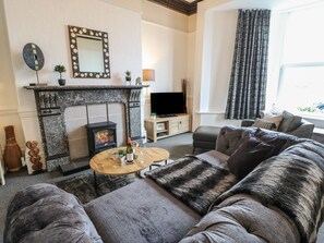 A living room with a fireplace, sofa, television, and a window with curtains.