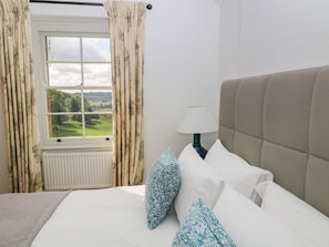 A bedroom with a bed, a window with curtains, a lamp, and a view of greenery.