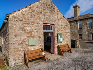 A stone building with a red door, wooden benches, and a gravel ground. - The Museum, Nenthead, Cumbria. (Alston)