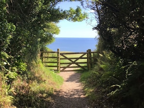 Ein Weg führt zu einem hölzernen Tor mit Blick auf das Meer.