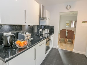 A modern kitchen with a black countertop, stainless steel appliances, and a dining area with wooden chairs.