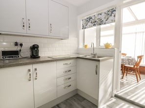 A kitchen with white cabinets, a countertop, a sink, and a window with a floral curtain. - Sally's Berth, Scarborough (Scarborough)