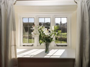Een uitzicht op een tuin, een bloemenvaas en een gordijn.