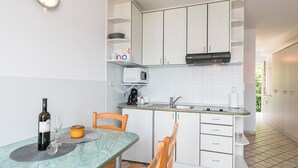 Ett kompakt kök med vita skåp, en mikrovågsugn, ett handfat och en matplats med stolar och ett bord.