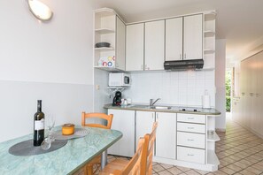 Eine kompakte Küche mit weißen Schränken, einer Mikrowelle, einem Spülbecken und einem Essbereich mit Stühlen und einem Tisch.