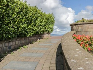 A paved pathway flanked by a hedge and a brick wall with a flower bed. - Eden on the Crescent, Morecambe (Morecambe)