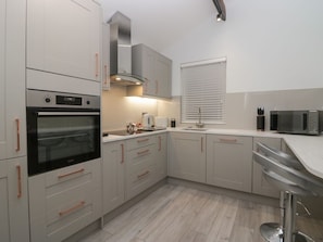 A modern kitchen with grey cabinets, a built-in oven, a microwave, and a window with blinds. - Eden on the Crescent, Morecambe (Morecambe)