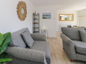 A living room with two grey sofas, a white chair, a shelf with decorative items, a painting, and a mirror. - GaGa Ar y Traeth, Morfa Bychan (Porthmadog)