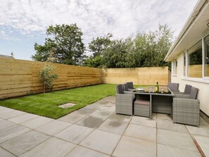 A patio with a table and chairs, a wooden fence, and a grassy lawn. - GaGa Ar y Traeth, Morfa Bychan (Porthmadog)