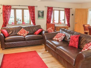 Ein Wohnzimmer mit zwei braunen Ledersofas, roten Kissen mit Muster und einem roten Teppich. Eine Holztür ist ebenfalls zu sehen.