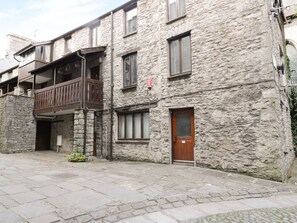 A stone building with a wooden balcony, a door, and a small garden area. - 11 Camden Building, Kendal (Kendal)