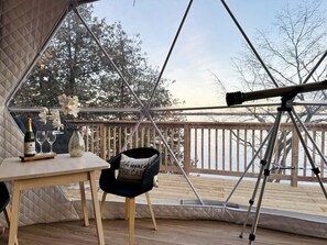A cozy room with a telescope, a table with a bottle and glasses, and a chair with a cushion.