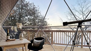 Una habitación acogedora con un telescopio, una mesa con una botella y vasos, y una silla con cojín.
