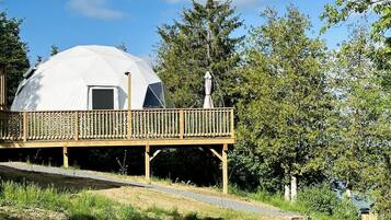 Une structure en forme de dôme géodésique, dotée d’une terrasse en bois et d’une petite statue.
