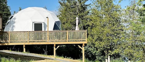 Une structure en forme de dôme géodésique, dotée d’une terrasse en bois et d’une petite statue.