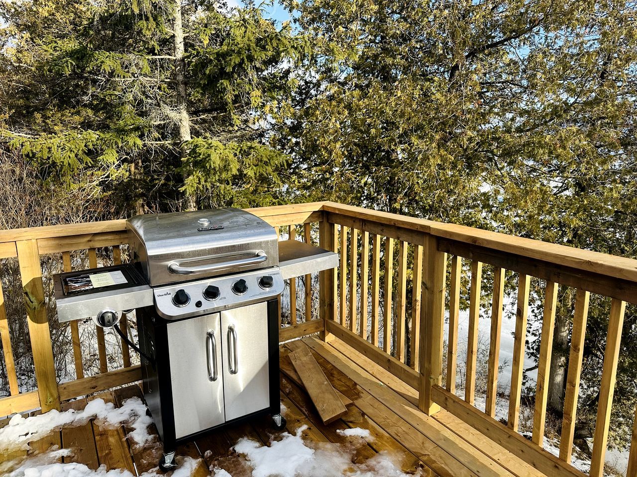 A barbecue grill on a wooden deck with snow on the ground.