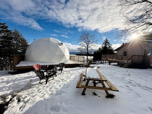 A geodesic dome structure, a wooden deck, and a picnic table in a snowy outdoor setting.