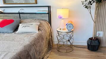 A bedroom with a bed, bedside lamp, clock, and a potted plant.