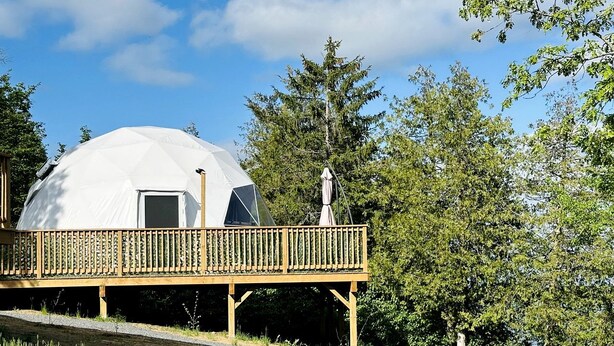 A geodesic dome structure with a wooden deck and a small statue.