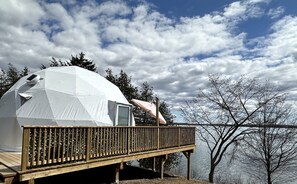 A geodesic dome structure with a wooden deck and a small enclosed area, overlooking a body of water and trees. - Stunning Dome with Barbecue and Great Vistas in Yarker, Ontario (Yarker)