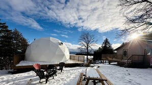 A geodesic dome structure, a wooden deck, and a picnic table in a snowy outdoor setting.
