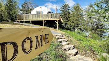 Un panneau en bois sur lequel est inscrit le mot « DOME », indiquant le chemin vers un bâtiment en forme de dôme, doté d’une terrasse en bois et offrant une vue sur des arbres et une étendue d’eau.