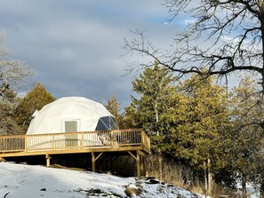 A geodesic dome structure with a wooden deck and a door, surrounded by trees and snow. - Stunning Dome with Barbecue and Great Vistas in Yarker, Ontario (Yarker)