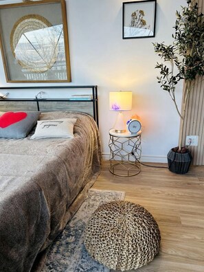 Un dormitorio con cama, lámpara de noche, reloj y planta en maceta.