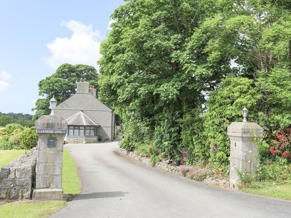 Ein Steinhaus mit einem Schild, auf dem 'Garnedd DDIU' steht, und einer gepflasterten Straße, die dorthin führt.